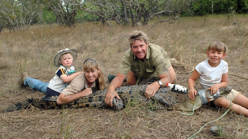 Two young children and two adults lying on the ground with a restrained crocodile.