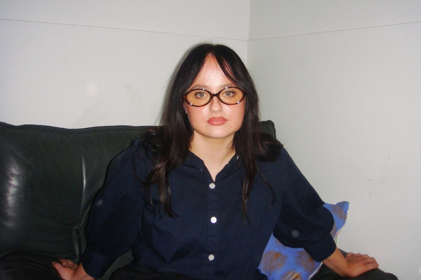 A young woman with brown hair and glasses on a couch