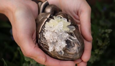 hands hold a small bronze sculpture of a human heart with crystals growing in the center of it