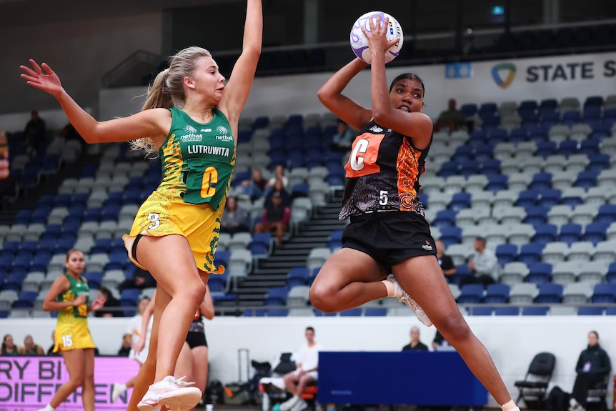 A netballer is mid air as she catches the ball, a defender is jumping nearby