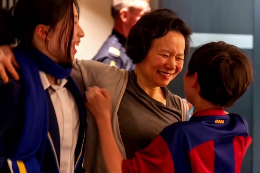A mother smiles big as her daughter and son excitedly embrace her for a hug.