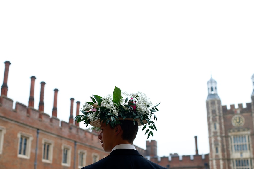 A boy wears a flower-laden boater in front of a building.