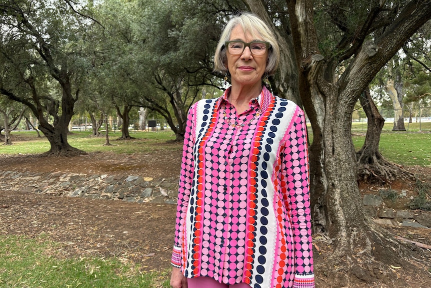 A woman in colourful top stands and smiles in front of a tree in a park