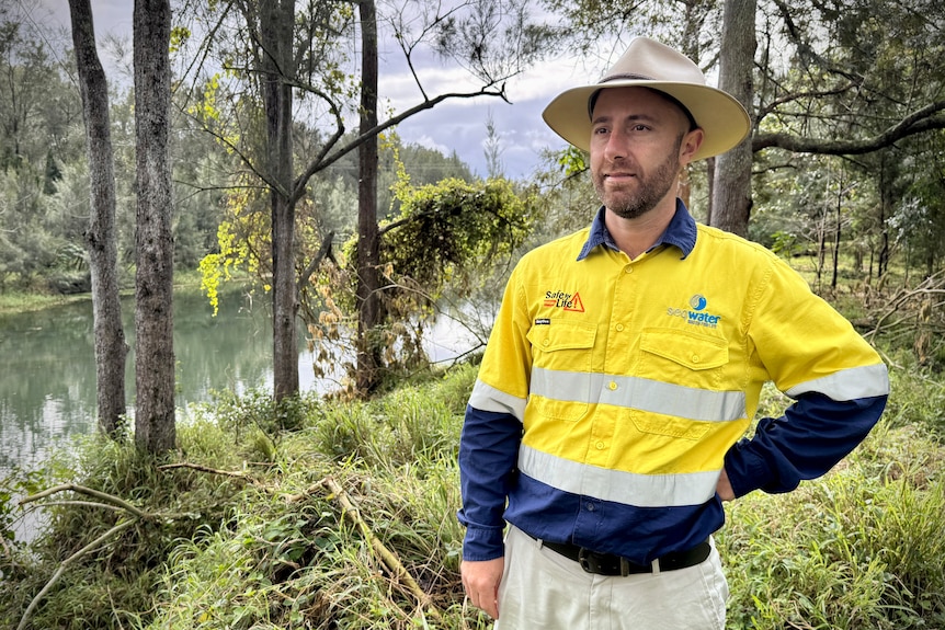 A man in a high vis yellow shirt and hat looks out towards the river.