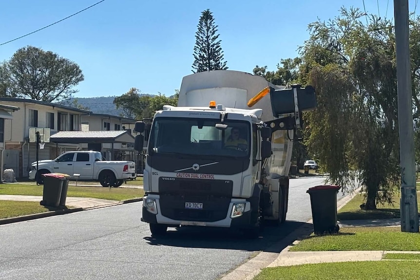 A rubbish truck empties a recycling bin on a street