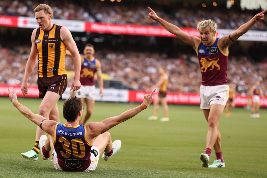 Two AFL players in red and blue have arms outstretched in celebration, player in yellow and brown behind