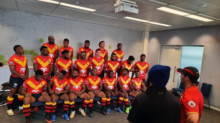A group of PNG rugby league players wearing black, red and yellow league jerseys set up to pose for a PNG sports photographer