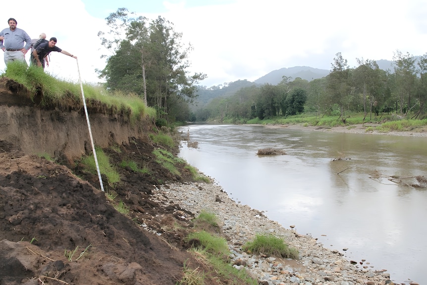Three men measuring the erosion drop down to a river.