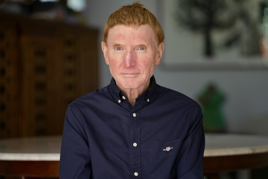 Man staring into camera lens in navy shirt blurred background