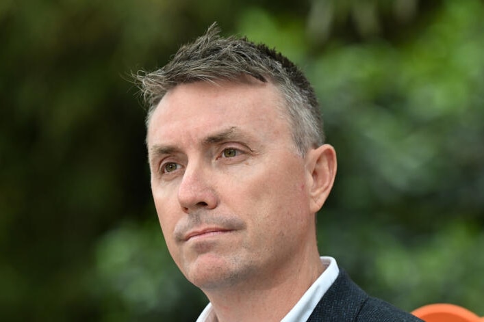 A close-up image of James Ashby looking serious with green shrubbery in the background.