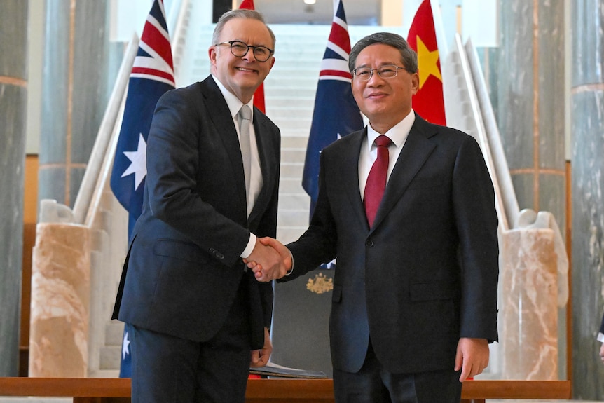Anthony Albanese wears a dark suit, smiles, and shakes hands with Li Qiang who is in a black suit.