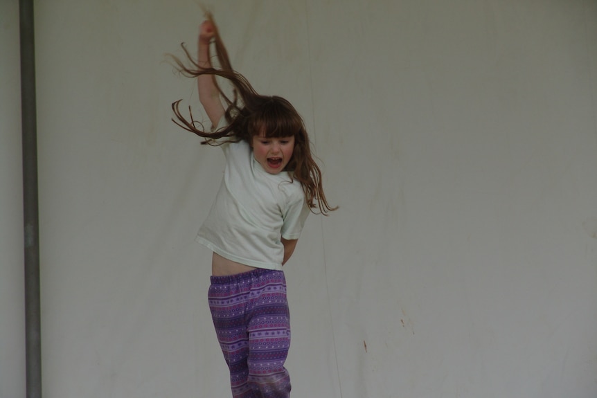 A five-year-old girl with long mousey brown hair and a fringe photographed jumping in the air.