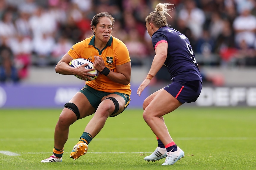 A pair of female rugby players face off on the field during a match.