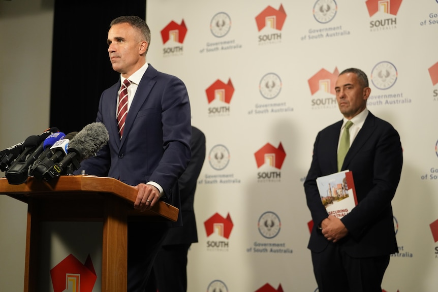 Peter Malinauskas standing at a lecturn giving a press conference with Tom Koutsantonis standing behind him