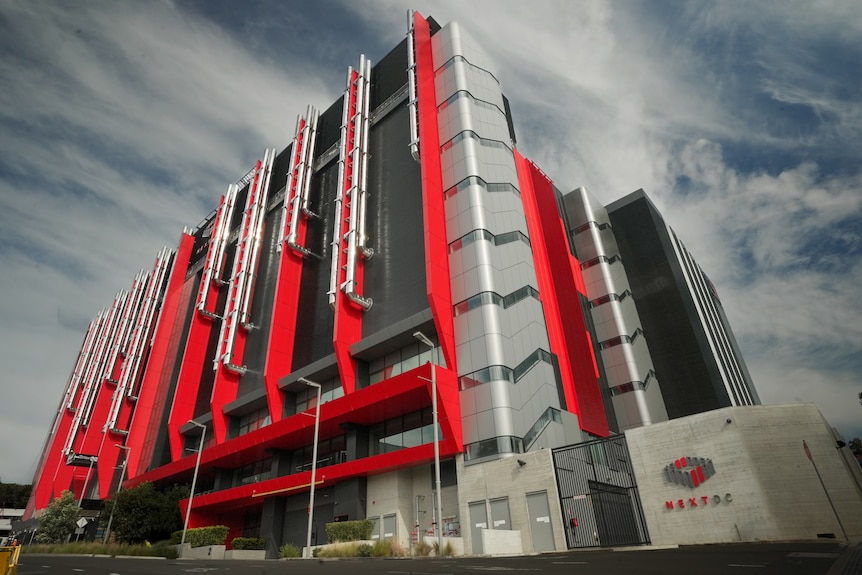 a towering building is covered in futuristic red panels and laced with large silver exterior pipes