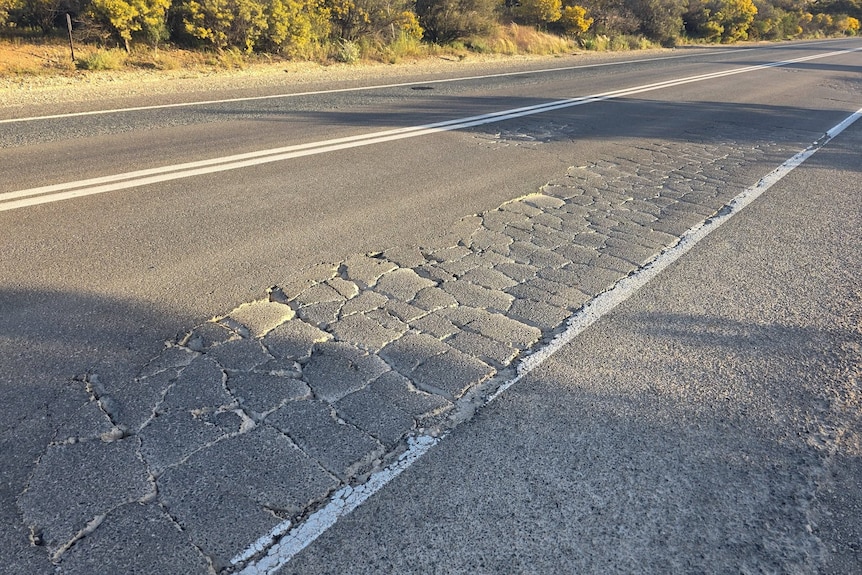 A sealed road with several cracks in it.