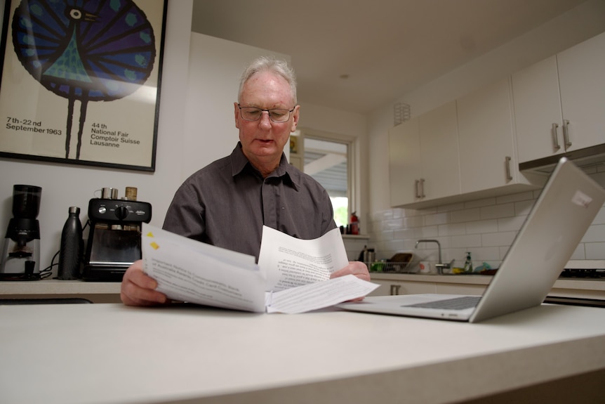 Man looks at a letter from the Commonwealth Bank, sitting at table with laptop open.