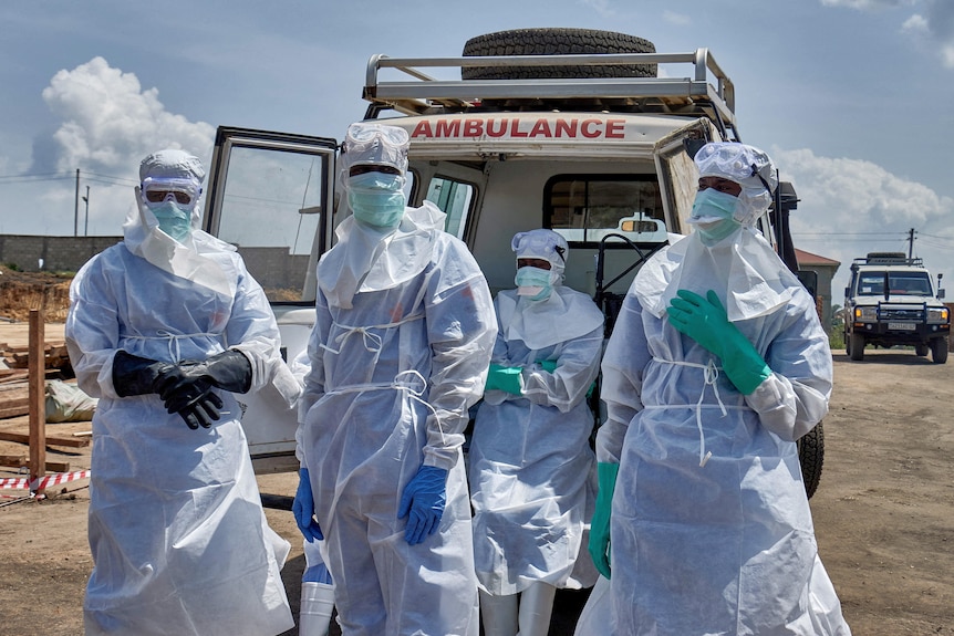 health care workiers in ppe and masks stand in front of an ambulance