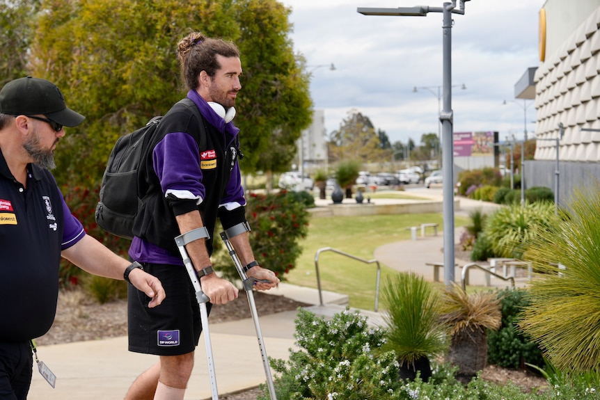  Alex Pearce dressed in team uniform uses crutches.