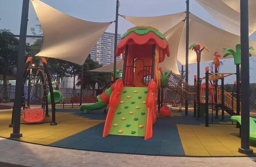 Colorful playground in Jakarta by Dream Garden, with slides, swings, and rope nets under white shade sails at dusk.