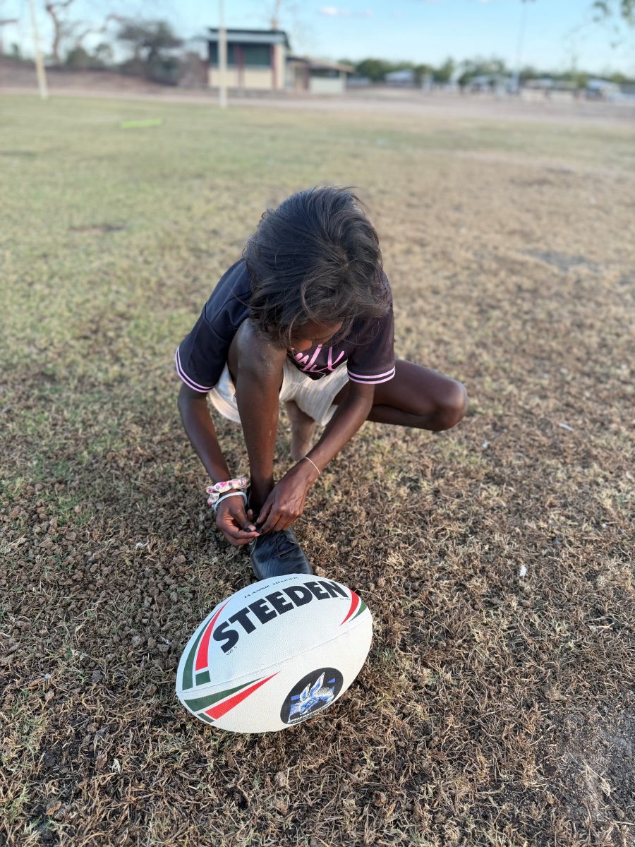 Aboriginal girl lacing up her boots for rugby league