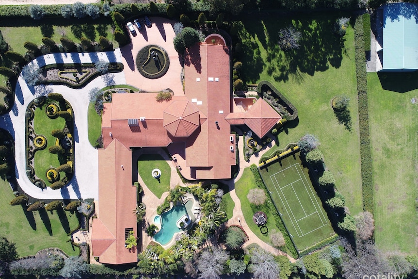 A birds eye view picture of a sprawling estate with a big property, pool, gardens, fancy driveway.