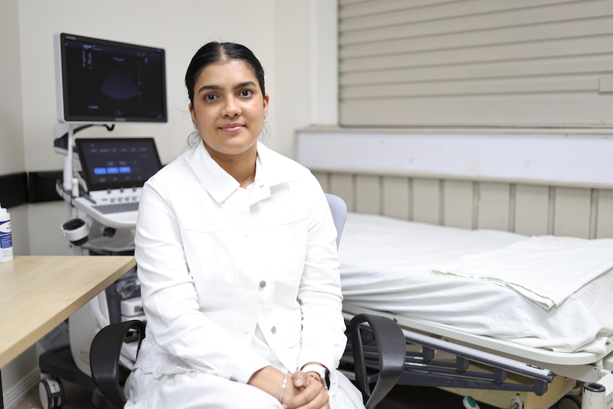A woman sits in front of a bed and monitor.