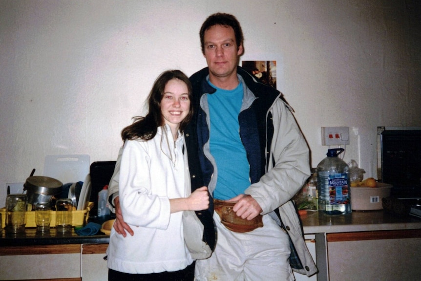 A young woman in a white shirt and a man in a blue shirt with a white jacket standing together.