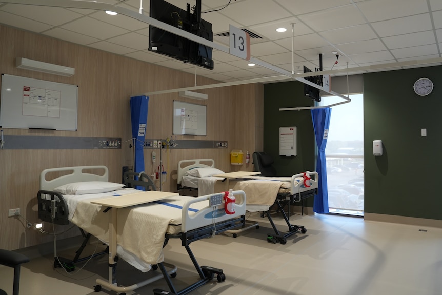 Two empty beds are stationed inside a room at Royal Darwin Hospital, there's a window nearby and a green feature wall.