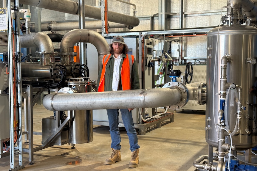 A man standing in the middle of a water processing plant surrounded by metal cylinders and pipes 