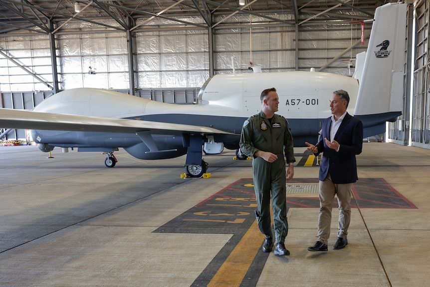 Richard Marles wears a suit and walks alongside Stephen Chappell in RAAF uniform, they talk and an aircraft is behind them.