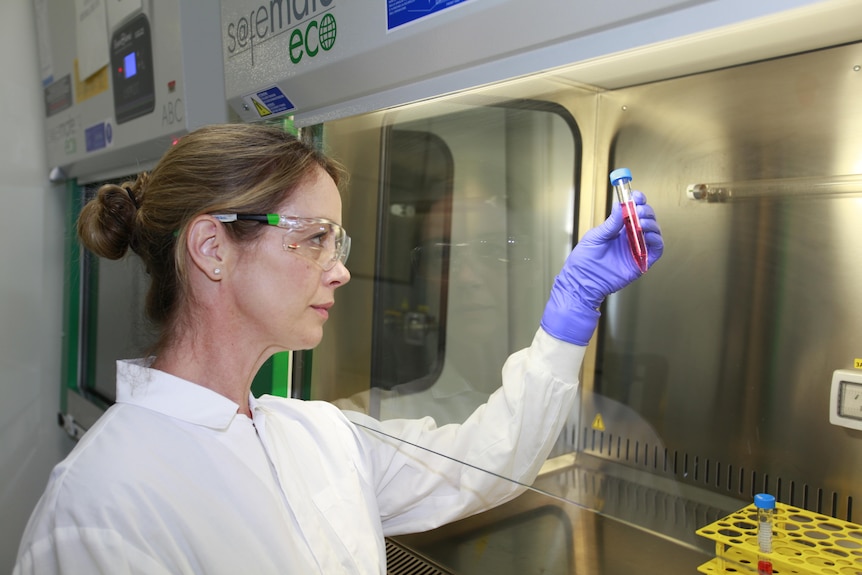 A woman in a lab coat holds up a test tube with red
