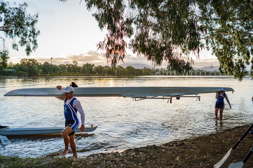 Two rowers carry a boat out to the riverbank