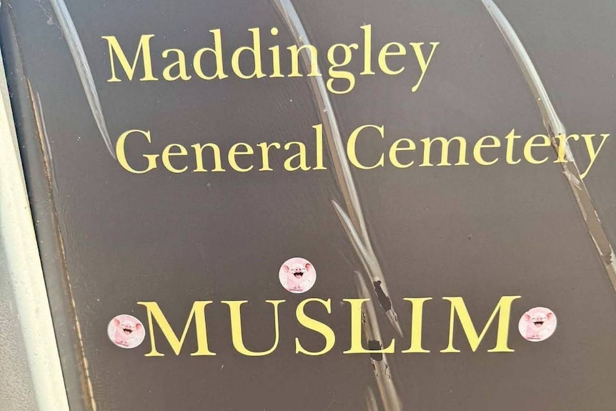 Three stickers of a pink cartoon pig are placed around the world "Muslim" on a sign for the Maddingley cemetery.