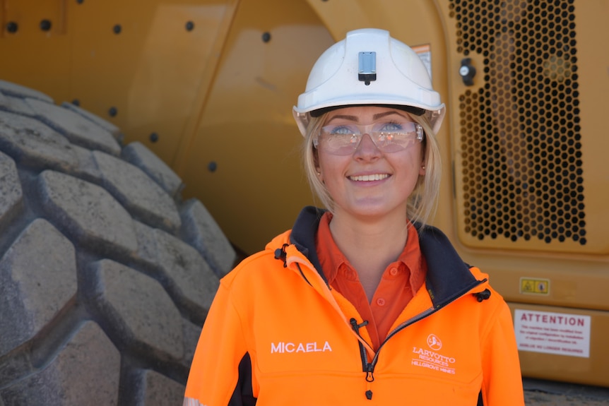 A blonde woman wearing high vis and a hard hat smiles into camera 