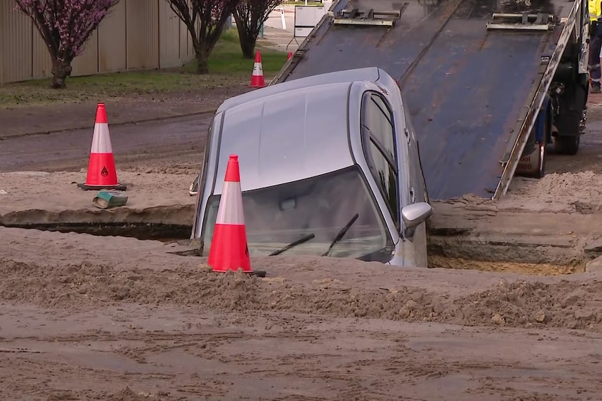 A front view of a car that has fallen into a sinkhole in the middle of the road