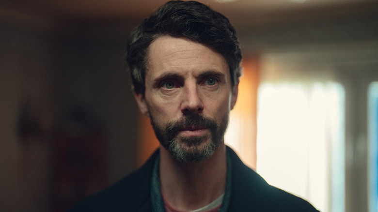Carl Morck (Matthew Goode) standing in a dimly lit room on 