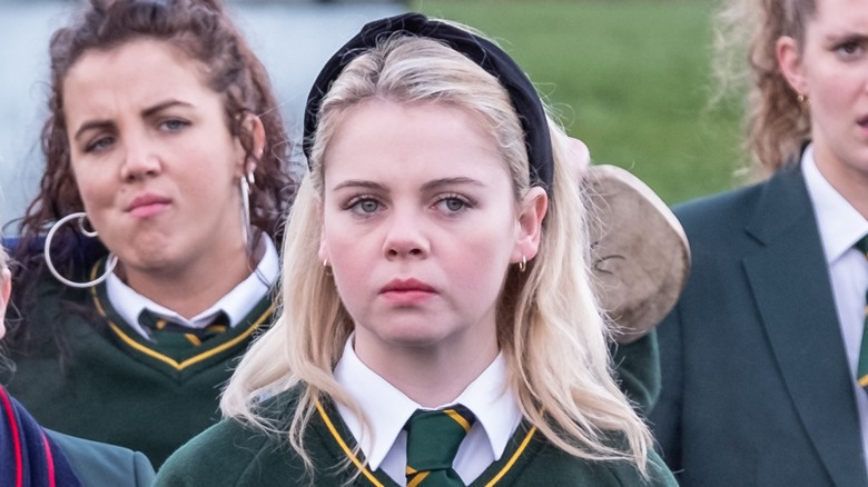 Erin wearing green school uniform in front of a crowd of students in similar outfits in 