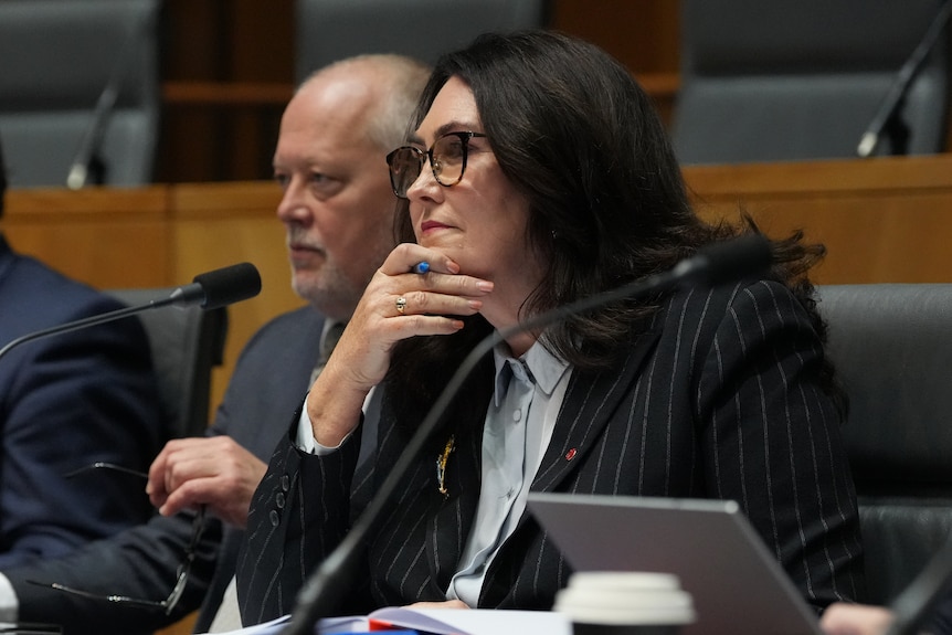 Senator Deborah O'Neill rests her hand on her chin as she listens during a parliamentary hearing.