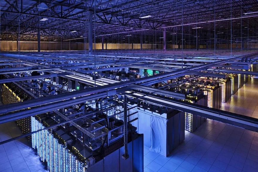 The dimly lit inside of a large warehouse looking down at rows of server racks.