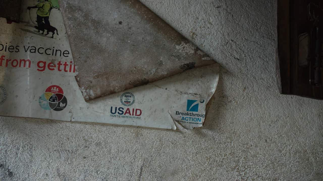A torn and weathered public health poster bearing the USAID logo remains partially attached to a rough concrete wall.