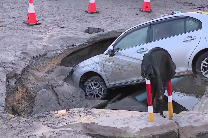 A silver car with the front half in a deep sinkhole.