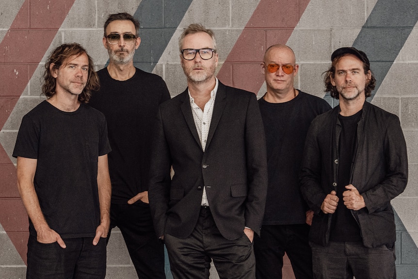The five members of The National pose for a photo outside a striped brick wall