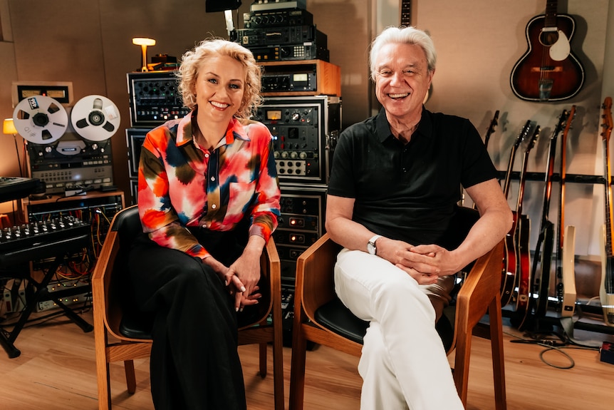 Zan Rowe and David Byrne seated in a recording studio, surrounded by guitars, tape machines and audio equipment.