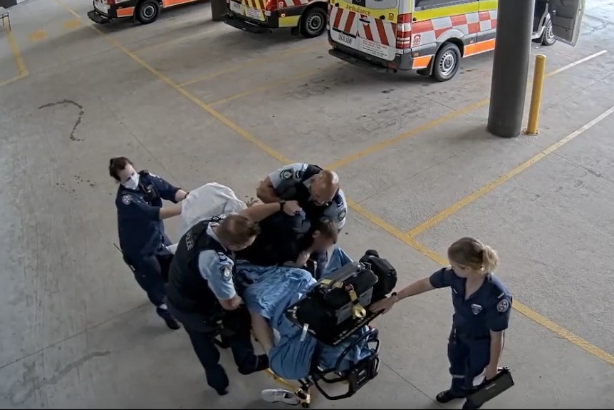Two police officers and two paramedics hovering around a man on a stretcher, ambos in the background.