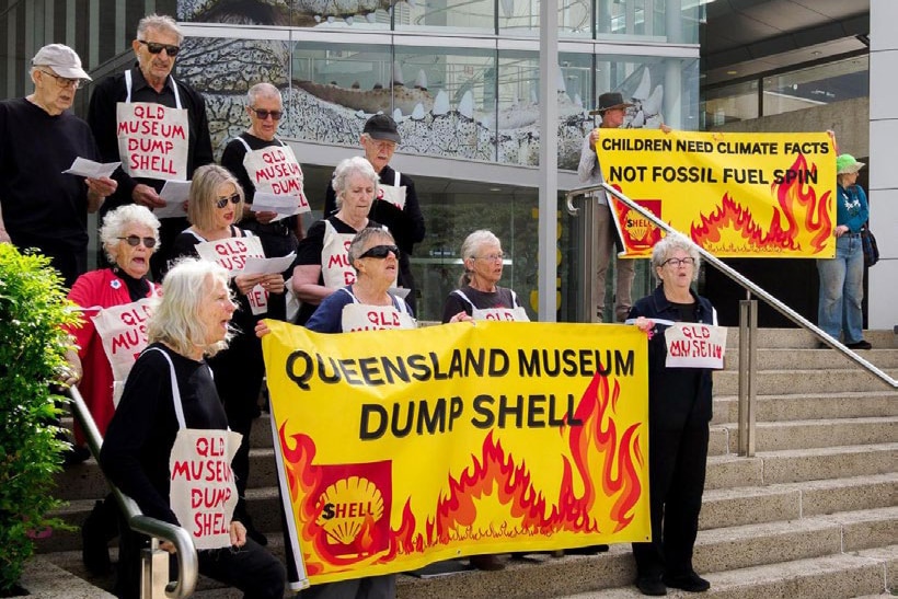 A group of mature people with 'Dump shell' signage protesting outside Queensland Museum.