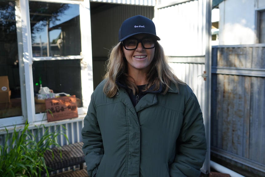 A woman in a cap stands in front of a shed.