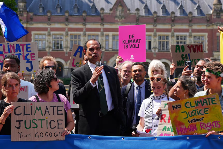 A man in a suit stands in a crowd behind a sign calling for climate justice