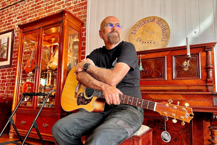 Image of a man resting a guitar on his lap, sitting at a piano.