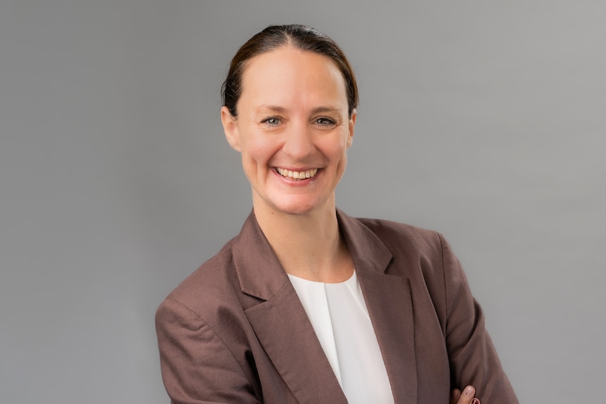 a woman in a brown blazer smiling with crossed arms